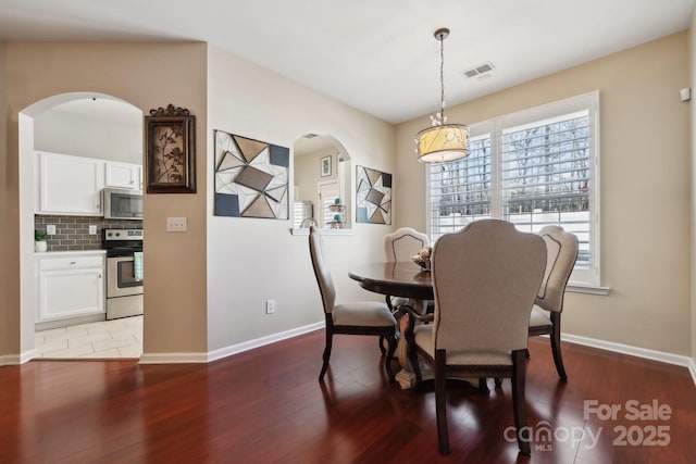 dining area with light wood-type flooring, visible vents, arched walkways, and baseboards