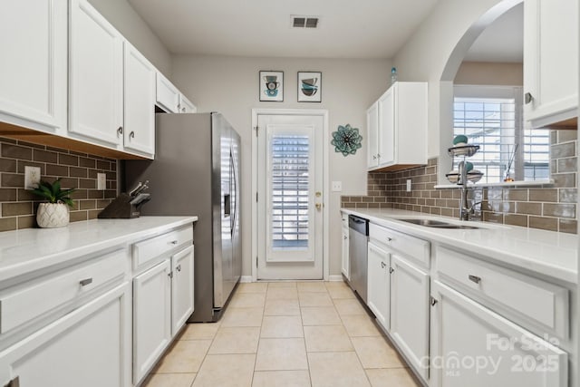 kitchen featuring arched walkways, light countertops, appliances with stainless steel finishes, white cabinetry, and light tile patterned flooring