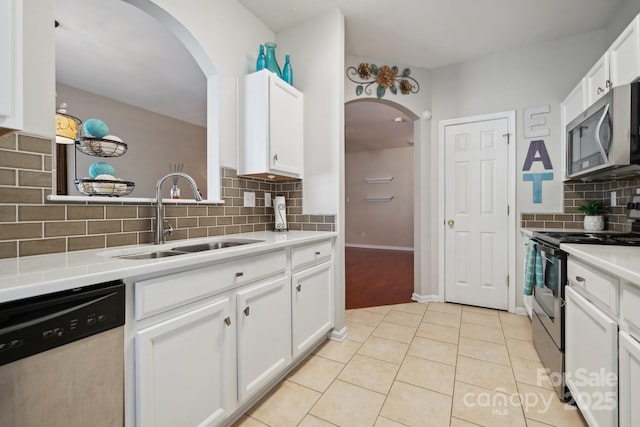 kitchen with light tile patterned floors, stainless steel appliances, light countertops, white cabinetry, and a sink