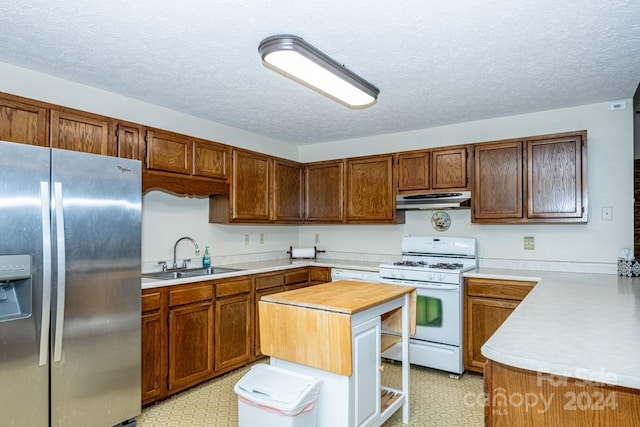 kitchen with stainless steel refrigerator with ice dispenser, gas range gas stove, a textured ceiling, sink, and a center island