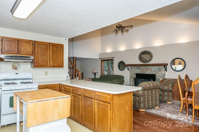 kitchen with gas range gas stove, ceiling fan, a stone fireplace, kitchen peninsula, and hardwood / wood-style floors