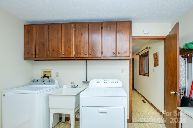 clothes washing area with washer and dryer, sink, cabinets, and a textured ceiling