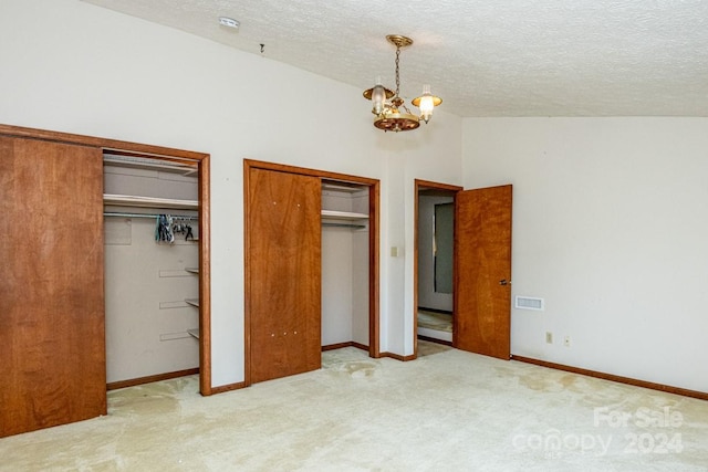 unfurnished bedroom featuring a textured ceiling, light carpet, a chandelier, and two closets