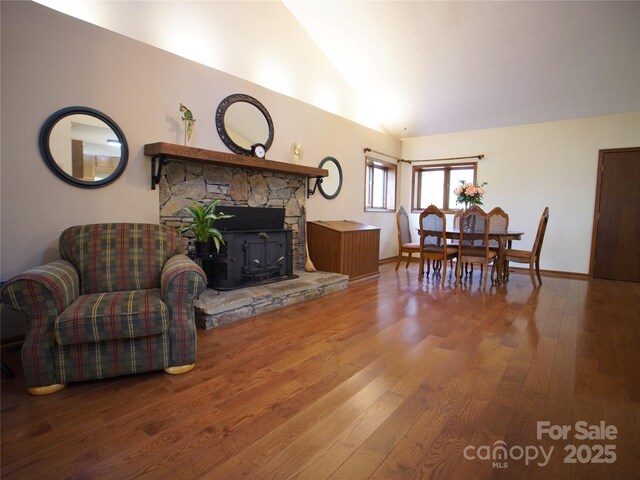living area with baseboards, vaulted ceiling, wood finished floors, and a wood stove