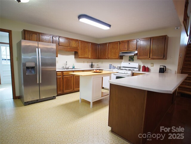 kitchen with a sink, a peninsula, stainless steel fridge, light countertops, and white gas range oven