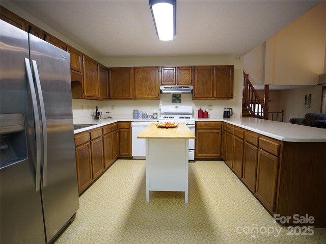 kitchen with a peninsula, white appliances, butcher block countertops, light floors, and under cabinet range hood