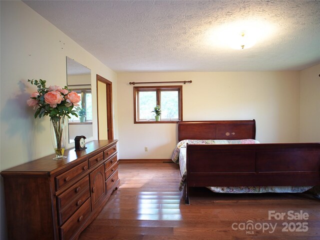 bedroom featuring baseboards, a textured ceiling, and wood finished floors