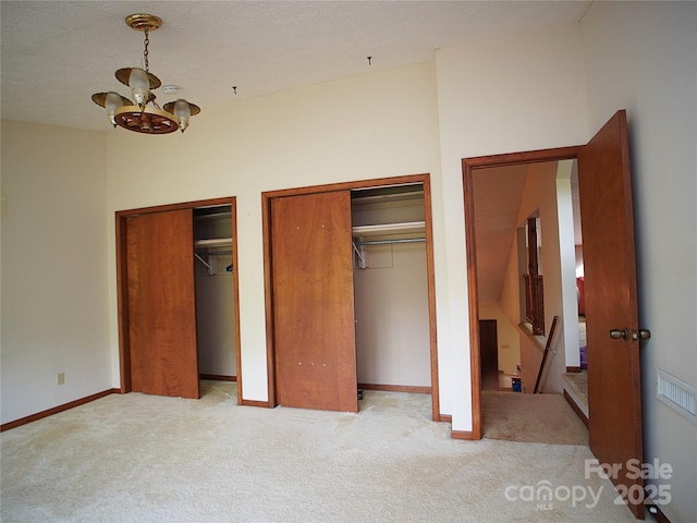 unfurnished bedroom featuring a notable chandelier, multiple closets, baseboards, and carpet