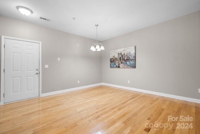 spare room with a notable chandelier and light wood-type flooring