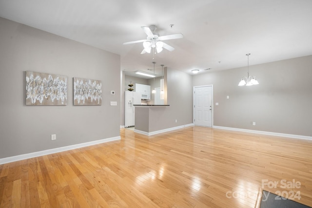 unfurnished living room featuring ceiling fan with notable chandelier and light wood-type flooring