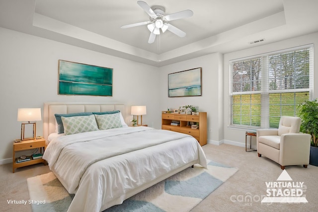 bedroom featuring ceiling fan, a raised ceiling, and light colored carpet