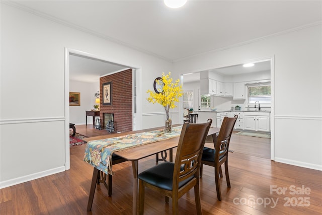 dining area featuring ornamental molding, sink, hardwood / wood-style floors, and a fireplace