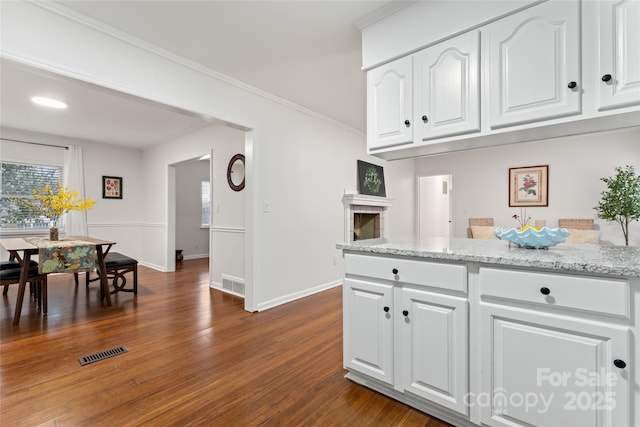 kitchen with light stone counters, ornamental molding, dark hardwood / wood-style flooring, and white cabinets