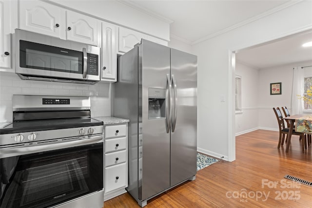 kitchen featuring tasteful backsplash, light hardwood / wood-style flooring, ornamental molding, stainless steel appliances, and white cabinets