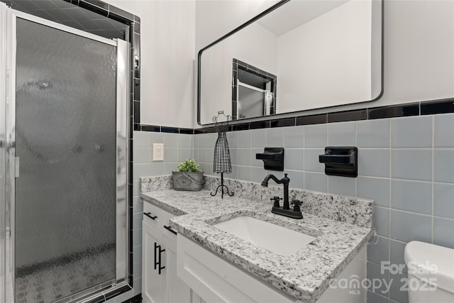 bathroom with a shower with door, vanity, tile walls, and toilet