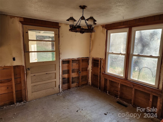 unfurnished dining area featuring a chandelier and a textured ceiling