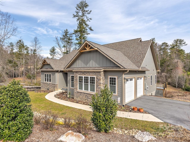 craftsman house featuring driveway, stone siding, a shingled roof, and board and batten siding