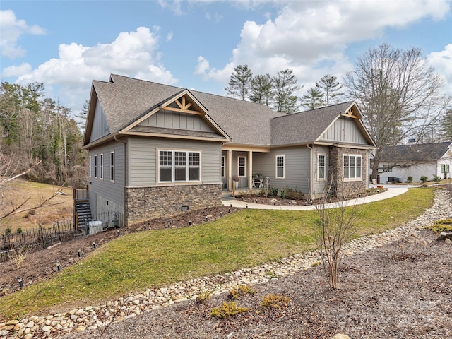 craftsman-style home featuring a shingled roof, board and batten siding, a front yard, fence, and stone siding