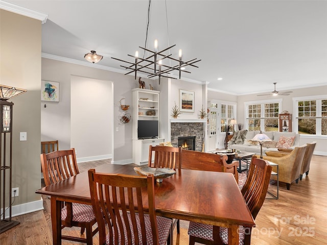 dining room with light wood finished floors, baseboards, ceiling fan, crown molding, and a fireplace