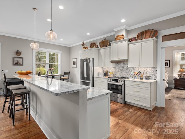 kitchen with under cabinet range hood, stainless steel appliances, dark wood-type flooring, a large island, and tasteful backsplash