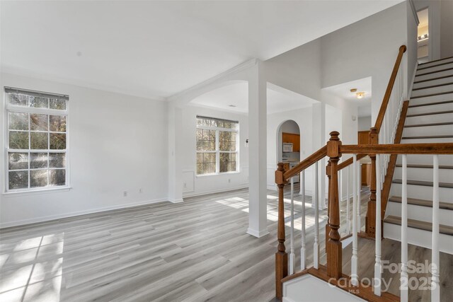 interior space with arched walkways, light wood finished floors, stairs, and baseboards