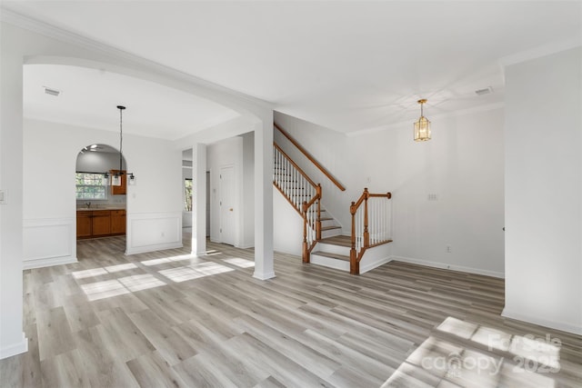 unfurnished living room with visible vents, light wood-style floors, an inviting chandelier, crown molding, and stairs