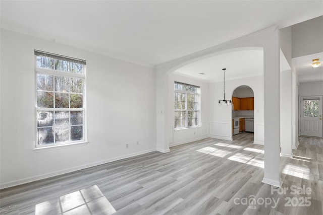 unfurnished room featuring arched walkways, plenty of natural light, crown molding, and light wood finished floors