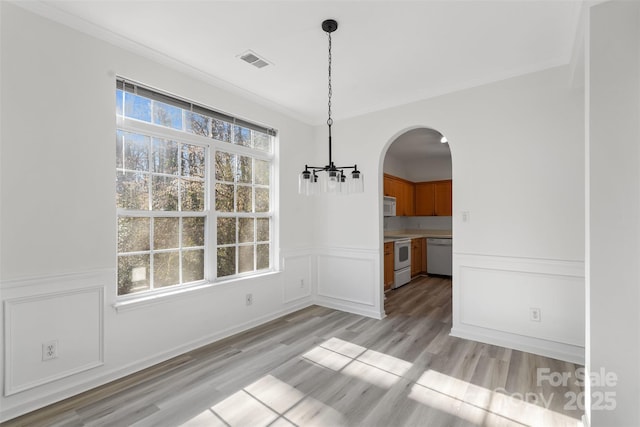 unfurnished dining area featuring visible vents, arched walkways, light wood-style floors, crown molding, and a chandelier