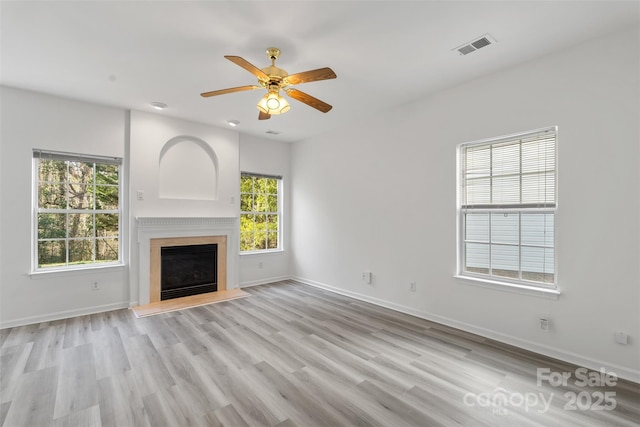 unfurnished living room with a ceiling fan, visible vents, baseboards, a fireplace with raised hearth, and light wood-type flooring