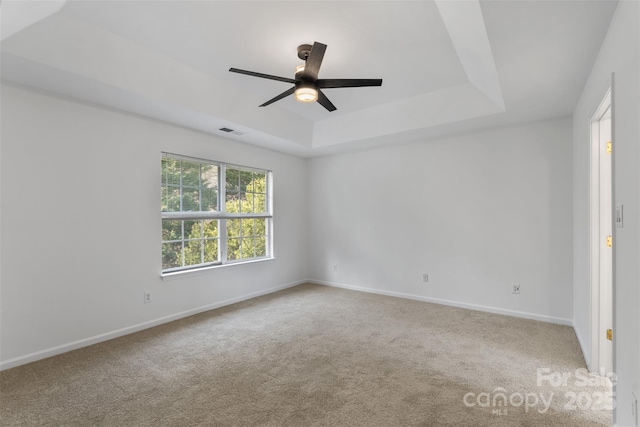 carpeted spare room featuring visible vents, a ceiling fan, a raised ceiling, and baseboards