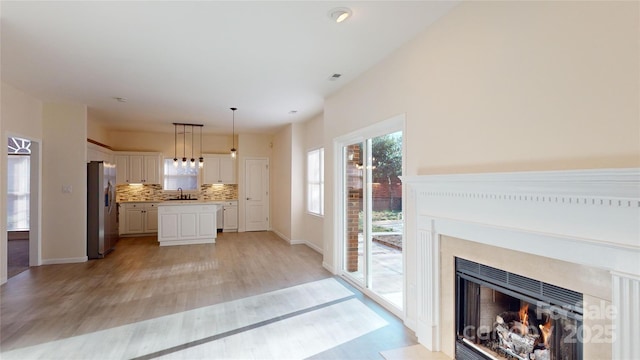 kitchen featuring stainless steel refrigerator with ice dispenser, tasteful backsplash, sink, white cabinets, and hanging light fixtures