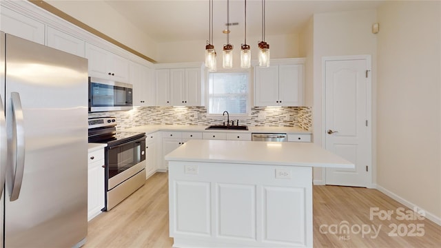 kitchen with appliances with stainless steel finishes, sink, pendant lighting, white cabinets, and a kitchen island