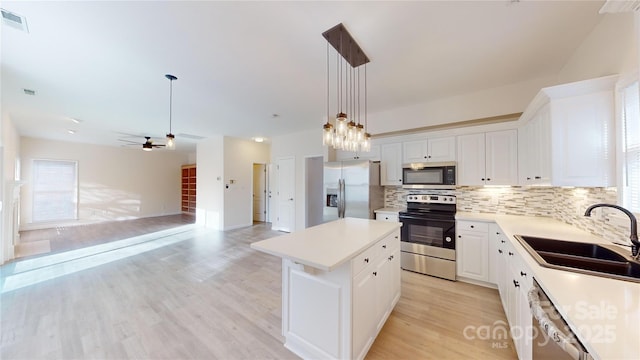 kitchen featuring sink, appliances with stainless steel finishes, decorative light fixtures, a kitchen island, and white cabinetry