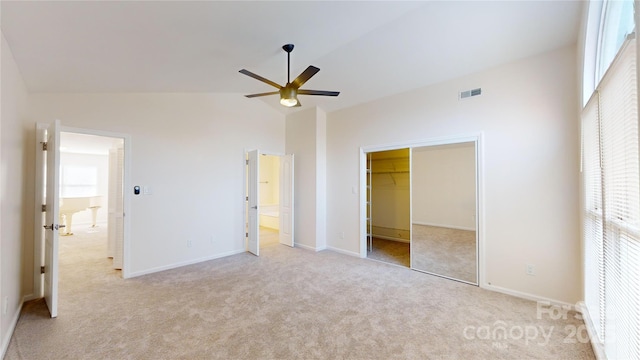 unfurnished bedroom featuring a walk in closet, light colored carpet, ceiling fan, a closet, and lofted ceiling