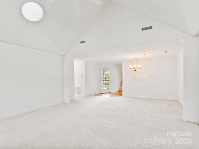 carpeted spare room with ceiling fan with notable chandelier and high vaulted ceiling