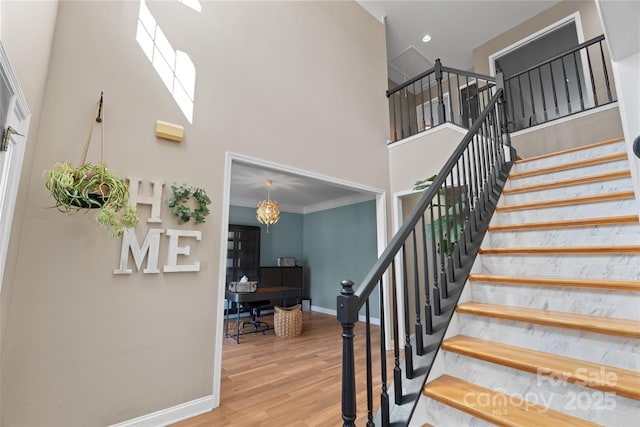 staircase with ornamental molding, wood-type flooring, a chandelier, and a high ceiling