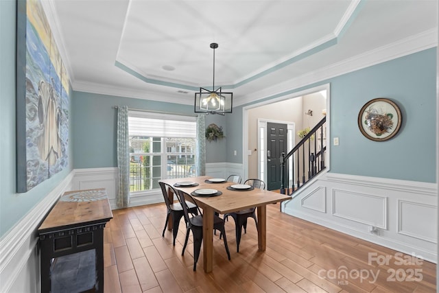 dining space with ornamental molding, a tray ceiling, hardwood / wood-style floors, and a notable chandelier