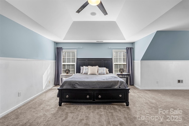 bedroom featuring ceiling fan, multiple windows, a tray ceiling, and light carpet