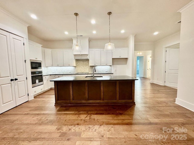 kitchen with sink, white cabinets, decorative backsplash, a kitchen island with sink, and stainless steel appliances