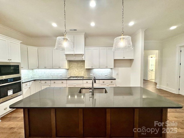 kitchen featuring stainless steel appliances, sink, a center island with sink, and white cabinets