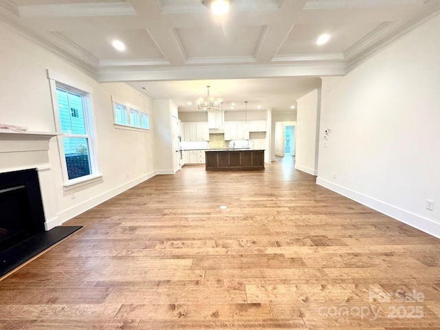 unfurnished living room featuring coffered ceiling, crown molding, light hardwood / wood-style floors, and an inviting chandelier