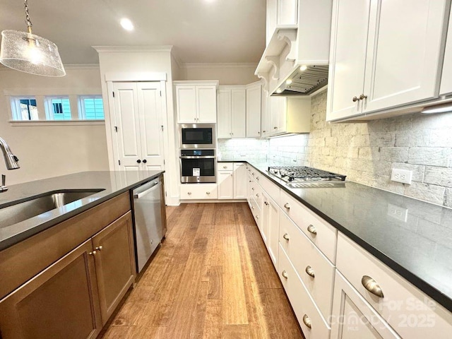 kitchen with sink, hanging light fixtures, stainless steel appliances, custom range hood, and white cabinets