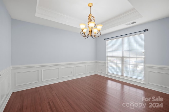 empty room with a tray ceiling, crown molding, an inviting chandelier, and hardwood / wood-style flooring