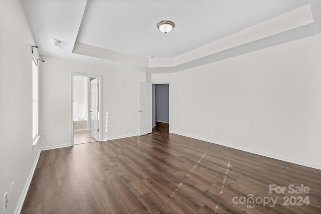 unfurnished bedroom featuring a tray ceiling, ensuite bath, and dark wood-type flooring