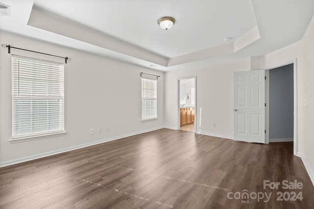 unfurnished bedroom featuring dark hardwood / wood-style flooring, ensuite bathroom, and a raised ceiling