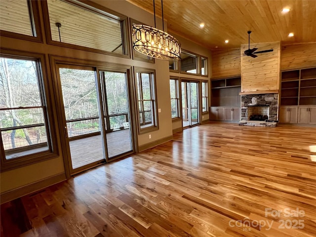 unfurnished living room with a stone fireplace, ceiling fan with notable chandelier, hardwood / wood-style floors, high vaulted ceiling, and wooden ceiling