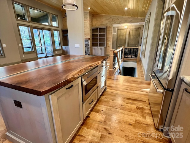 kitchen featuring butcher block counters, vaulted ceiling, appliances with stainless steel finishes, a kitchen island, and light hardwood / wood-style floors