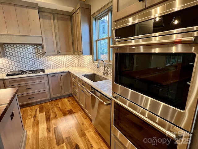 kitchen with sink, backsplash, light stone counters, stainless steel appliances, and light wood-type flooring