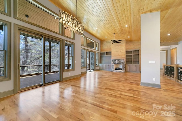 unfurnished living room featuring light wood-style floors, wood ceiling, built in features, and a stone fireplace