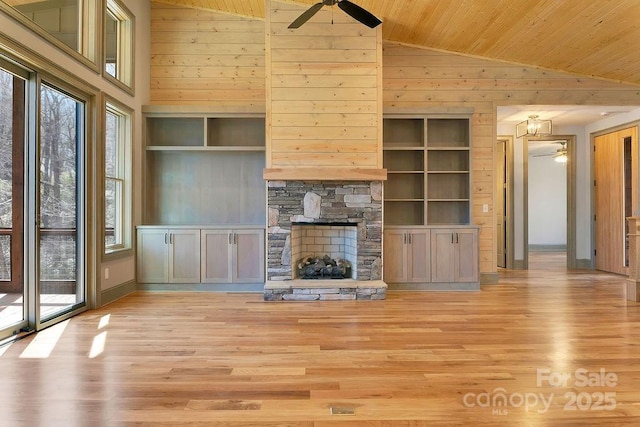 unfurnished living room with ceiling fan, wooden walls, a wealth of natural light, and a stone fireplace